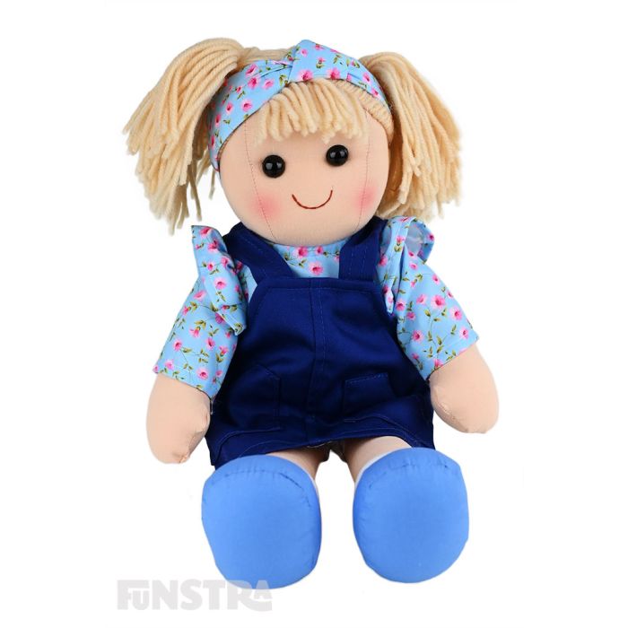 Carrie is a beautiful doll with a soft cloth body and blonde hair tied back in pigtails and wears a blue pinafore dress over a floral top and a matching headband.