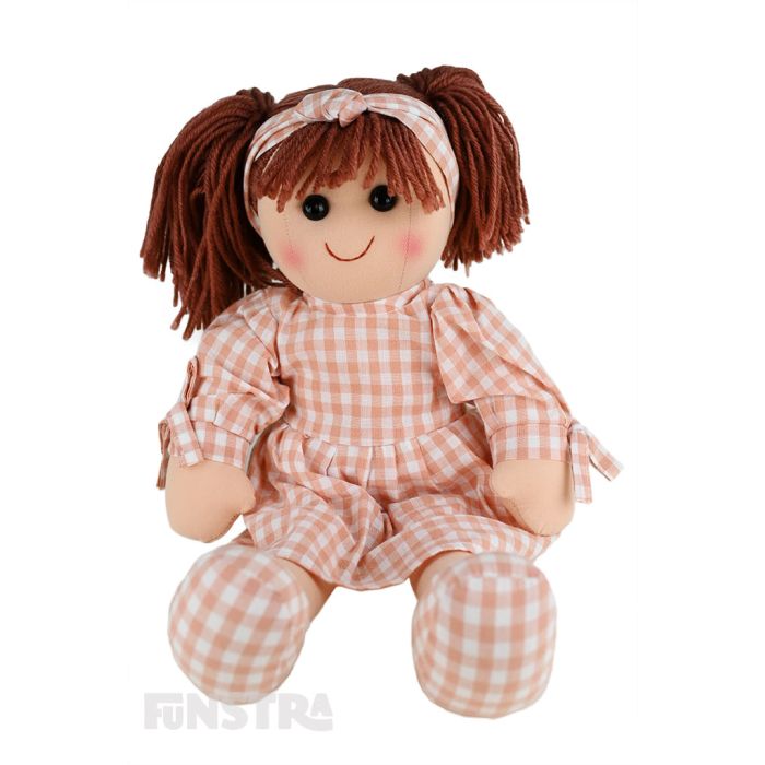 Sadie is an down to earth doll with a soft cloth body and brown hair tied back in pigtails and wears a peach printed dress featuring a gingham pattern and a matching headband.